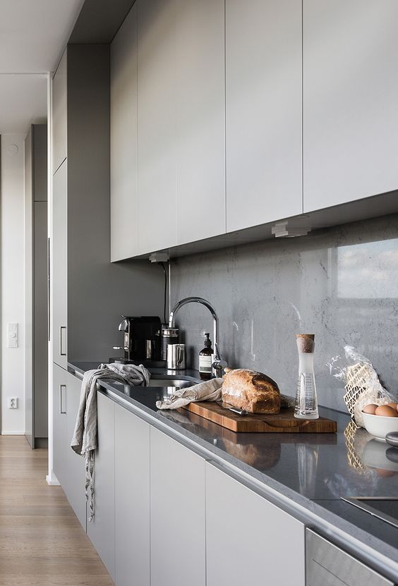 a minimalist grey kitchen with a concrete backsplash covered with a glass screen completely for keeping it clean