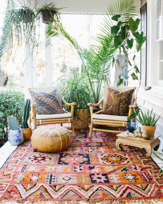a chic boho porch with potted greenery, succulents, rattan furniture, a boho rug and a lather ottoman