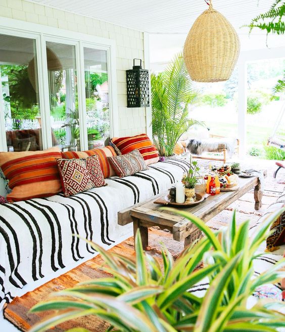 a colorful boho porch with a wicker lampshade, printed and colorful textiles, potted greenery and lanterns