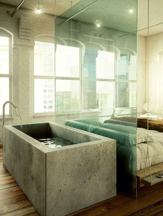 a industrial bedroom with a concrete bathtub separated with a glass divider from the bed