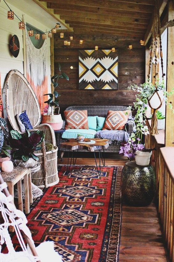 a colorful boho porch with rattan furniture, a sofa, a hammered side table, potted plants and a colorful geo artwork