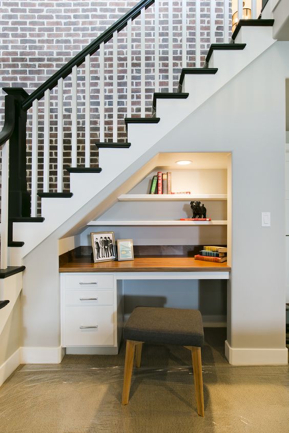 a little built-in home office nook with a built-in desk and shelves and lights and a small stool
