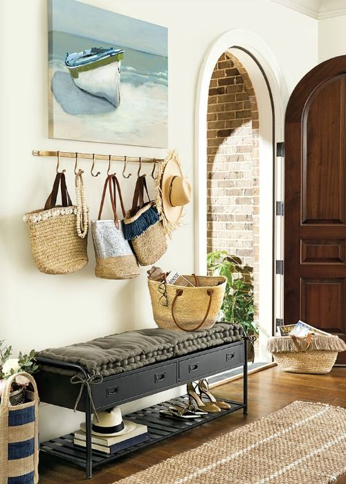 a coastal entryway with a watercolor boat artwork, an upholstered bench, some straw bags as part of decor