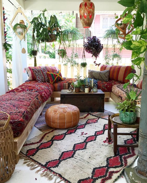 a colorful porch with a comfy lounge area, hanging potted greenery, lanterns, rugs and a wooden chest as a side table
