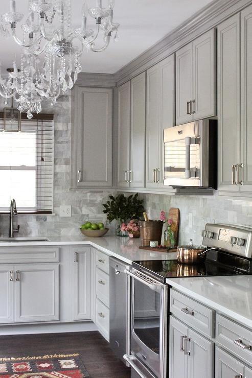 a traditional grey kitchen with glam touches like a crystal chandelier and a grey marble tile backsplash