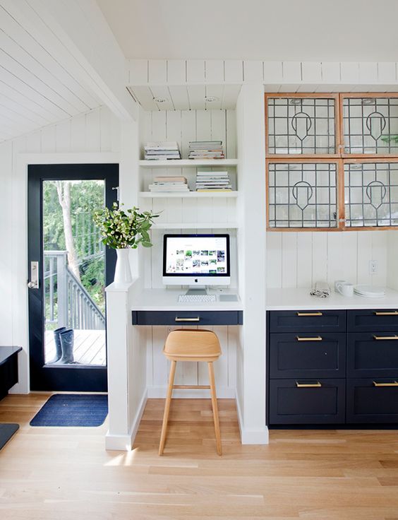 a stylish navy and white kitchen with a separated tiny office nook space with a built-in desk and shelves and a stool