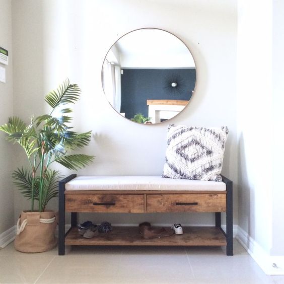 a wooden bench with metal legs and drawers, pillows, a mirror and a palm tree in a basket planter