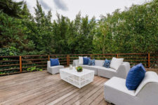 The deck features comfy upholstered furniture and there’s lush greenery all arond the space