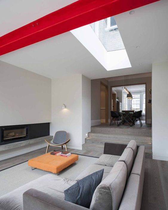 a minimalist space with a sunken living room accented with a bold red beam and an orange ottoman