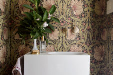 The mudroom is done with bold printed wallpaper, a floating sink and a chic mirror