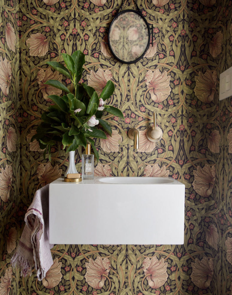The mudroom is done with bold printed wallpaper, a floating sink and a chic mirror