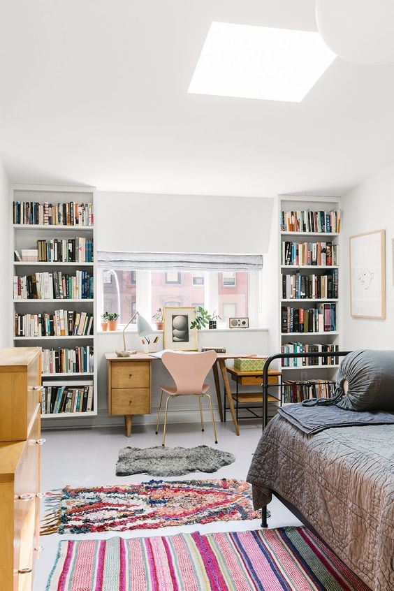 a guest bedroom with a home office space with bookcases and a wooden desj by the window for comfortable working