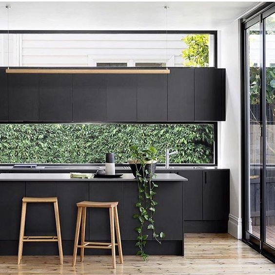 a matte black industrial kitchen with a window backsplash, the greenery seen through the window refreshens the space
