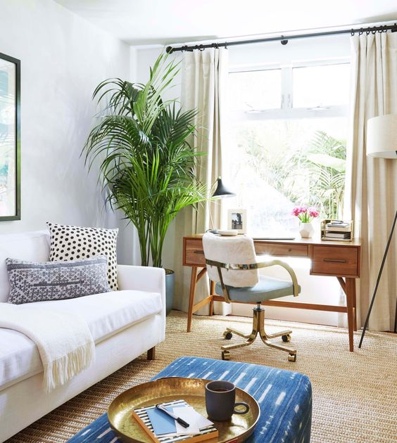 a modern boho space with a convertible sofa and a mid-century wooden desk by the window