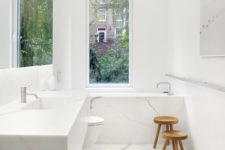 18 a minimalist white marble bathroom with a narrow window and a couple of wooden stools