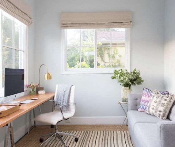 a small yet clean home office with a wooden trestle leg desk by the window and a grey sofa that can become a bed