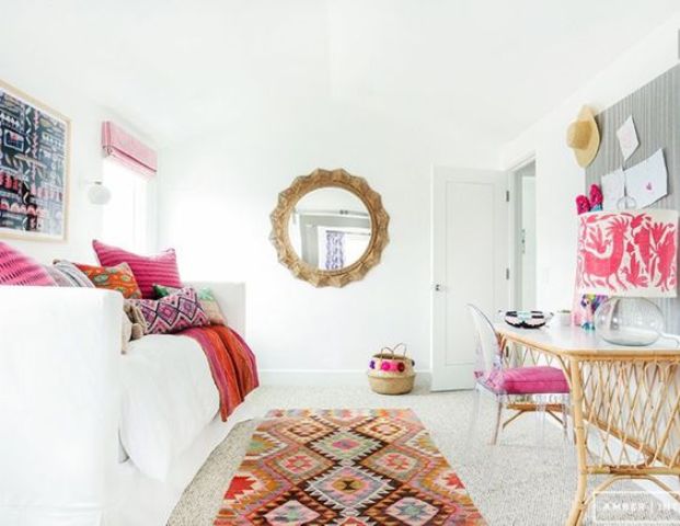 an adorably colorful guest bedroom with a convertible sofa and a wicker desk plus a pink chair