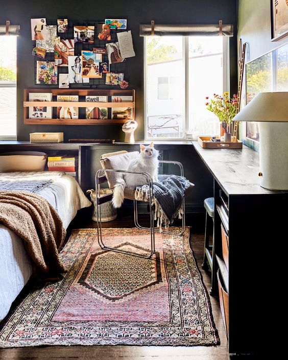 a black guest bedroom with a galleyr wall and a shelf with magazines, a corner desk with storage and a bed with bedding