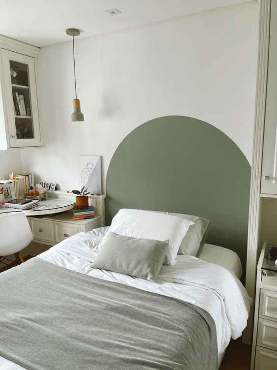 a cool guest bedroom with a bed and a painted headboard, a storage unit, a desk in the corner and some more cabinets