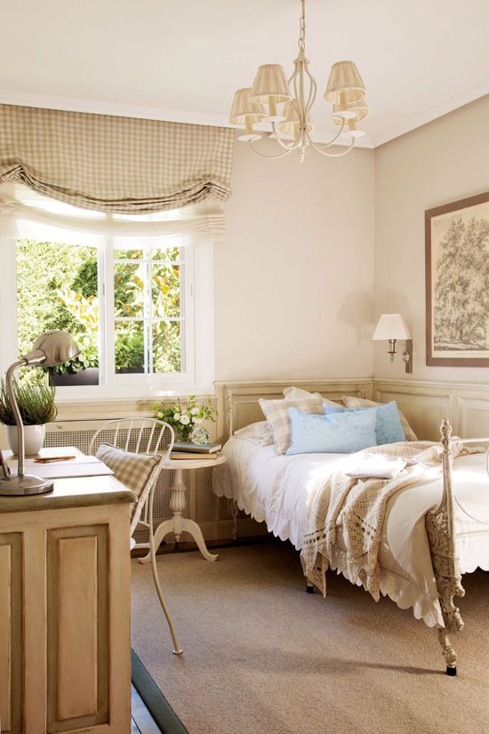 a lovely vintage guest bedroom with a bed with neutral bedding, a neutral desk and a forged chair, a side table and a chic chandelier