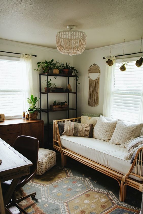 a small boho guest bedroom with a metal shelving unit, a stained dresser, a rattan bed with pillows, a desk and a chair, some boho decor