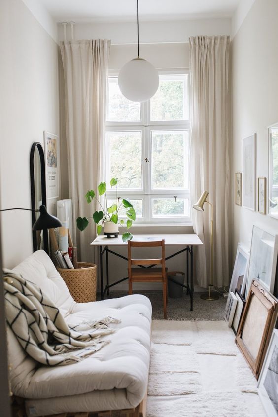 a small guest bedroom with a catchy sofa, a gallery wall, a small desk and a stained chair, a basket and a mirror