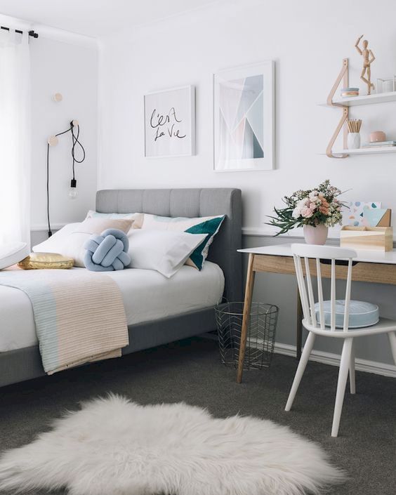 a stylish modern guest bedroom with a grey upholstered bed and pastel bedding, a desk and a chair, suspended shelves and layered rugs