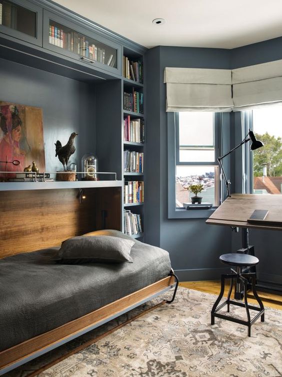 a vintage slate blue guest bedroom with built-in bookcases and a Murphy's bed, a desk and a stool