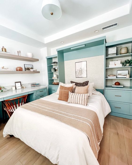 a welcoming guest bedroom with a mint blue storage unit and a Murphy's bed, a matching desk, open shelves