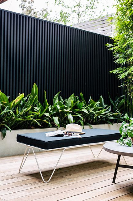a black wooden plank fence is combined with a large planter with greenery for a lively feel