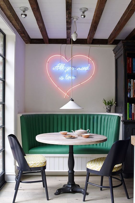 a bright dining space with a green banquette seating and a gorgeous neon sign