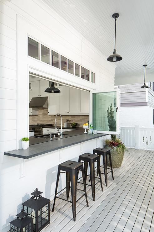 a kitchen pass through is fitted with glass folding windows fitted with a black bar lined with black stools