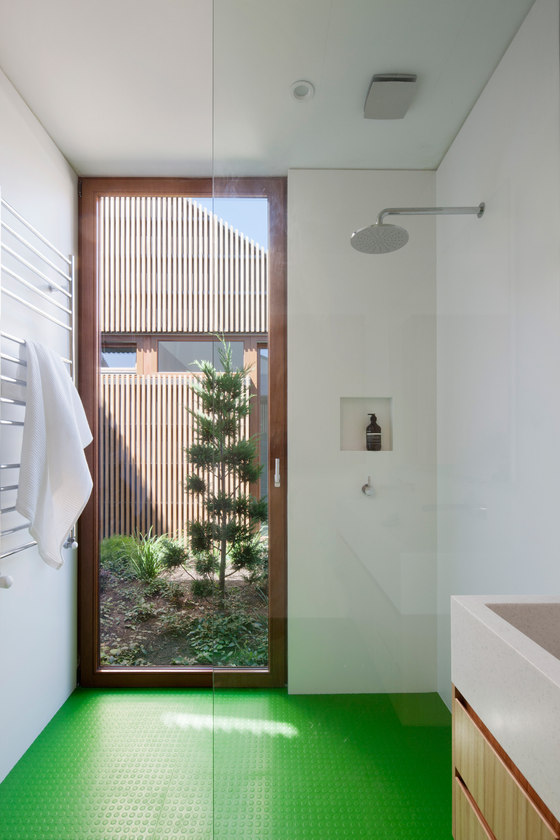 The bathroom features a floor to ceiling window door and a bright green floor in the shower