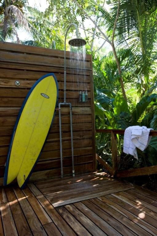 an outdoor shower totally clad with wooden planks and a surf as a decoration