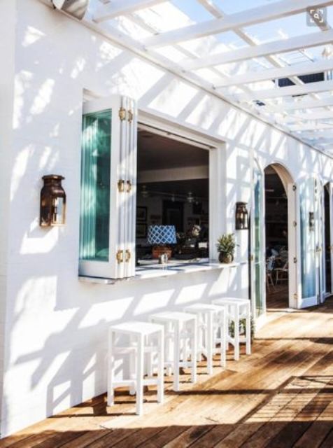 a tropical space with a folding window, a concrete bar counter and white wooden stools