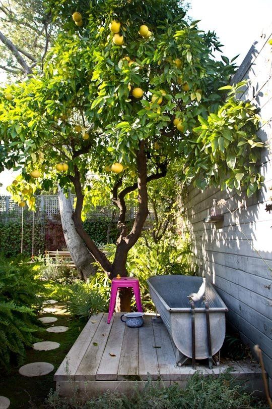 a tall wooden wall for privacy goes down into a deck, a metal tub and a pink chair for having a bath