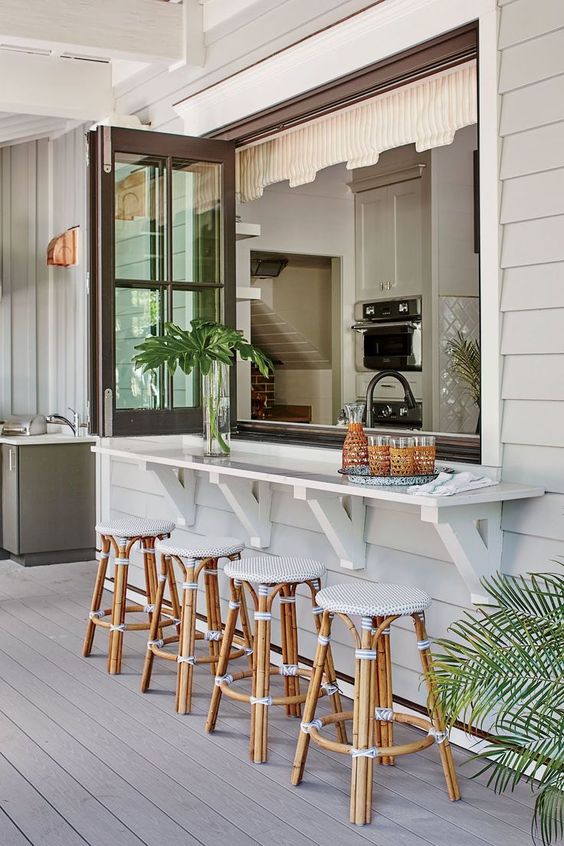 a tropical space with a folding window, a white bar counter and tropical stools of rattan and with upholstery