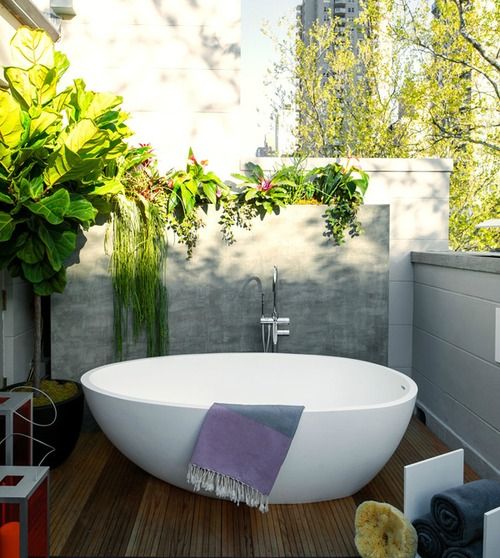 an outdoor deck with low walls all round to keep privacy yet have enough light, a stylish oval bathtub and lots of greenery