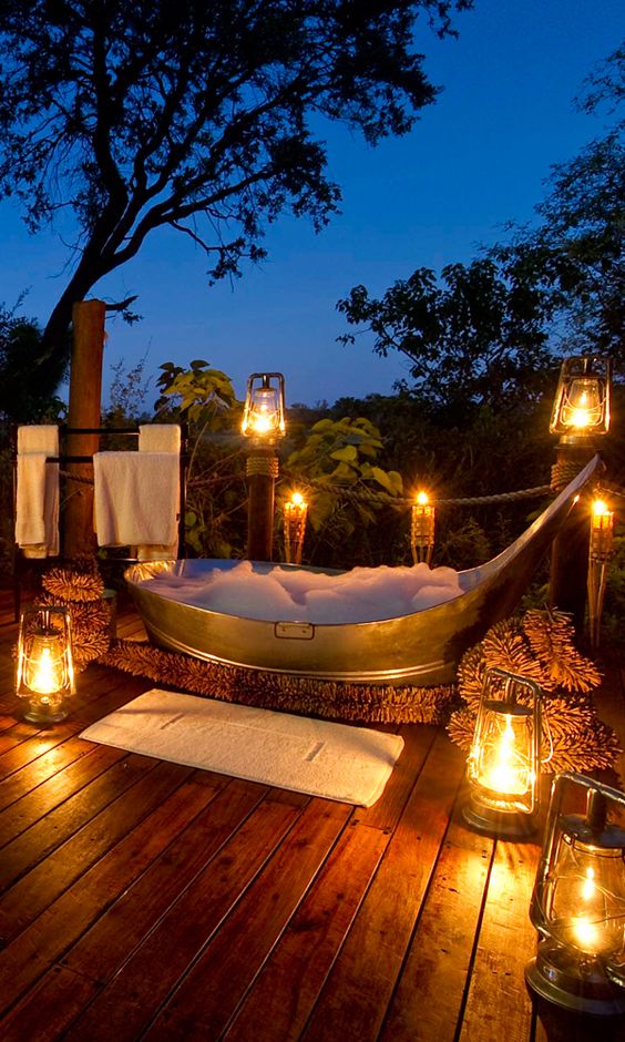 a dreamy outdoor space with lots of lanterns and a metal bathtub plus some textiles looks very welcoming