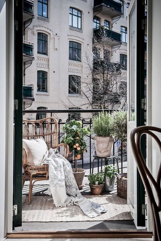 a small balcony with a wicker chair, potted greenery and baskets for storage