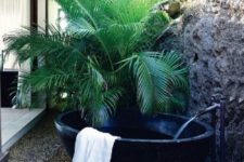 21 a simple yet gorgeous outdoor oasis with a potted palm, a black stone tub and pebbles on the ground