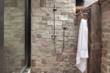 24 a small yet stylish outdoor shower clad with stone and bricks, a wooden deck and pebbles on the ground