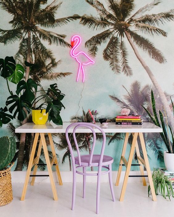 a colorful tropical home office space with palm wallpaper, a lilac chair and a pink flamingo neon light