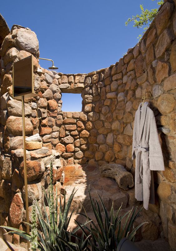 an outdoor rustic shower space all done with stone, potted plants and a window to enjoy the views