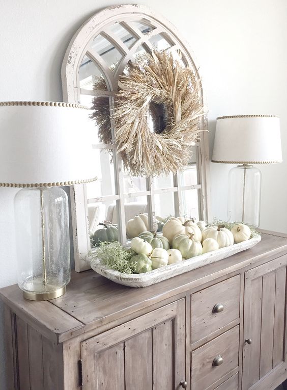 a farmhouse buffet with a corn husk wreath over the table and a tray with white and green pumpkins plus moss