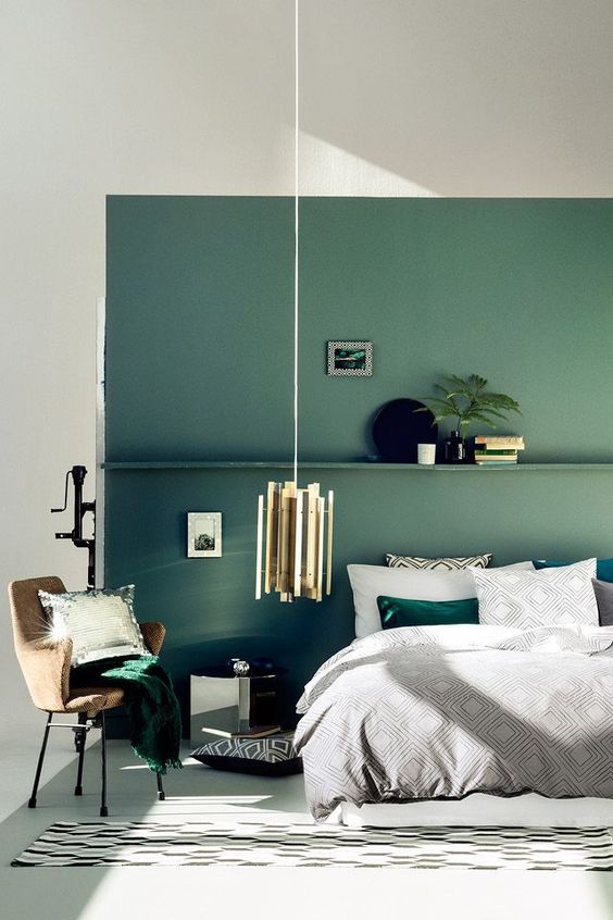 a muted green accent wall with a shelf and matching emerald bedding and a pillow