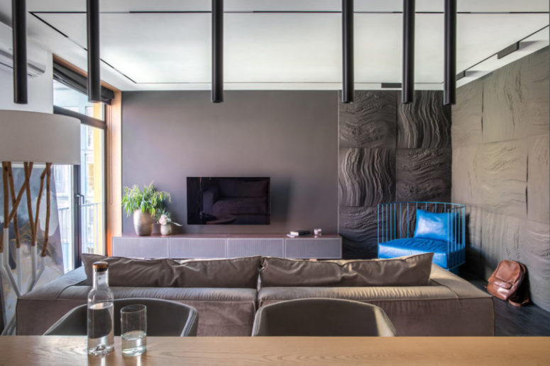 The living space is done with minimalist furniture, catchy stone-imitating wall panels and a bright blue chair for a colorful touch