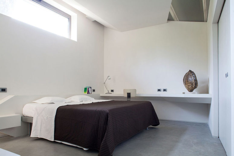 The master bedroom is done in white with acrhitectural geometric details, a metal bed and a floating desk or vanity The master bedroom is done in white with acrhitectural geometric details, a metal bed and a floating desk or vanity