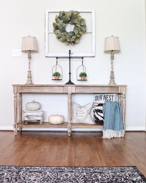 a fall farmhouse console table with white pumpkins, pillows and greenery in pots
