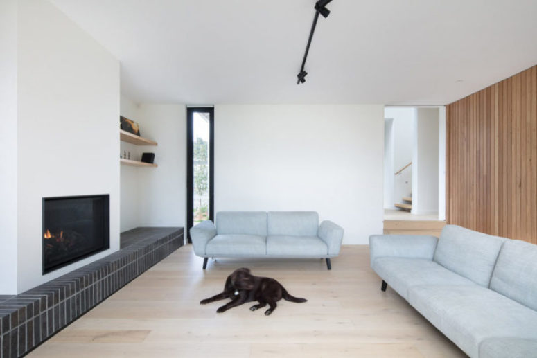 The living room is done with light grey sofas, a wood plank wall, a built in fireplace and some windows The living room is done with light grey sofas, a wood plank wall, a built-in fireplace and some windows